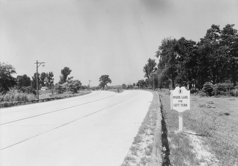 A new concrete highway curving past trees, with a sign reading Inside Lane for Left Turn.